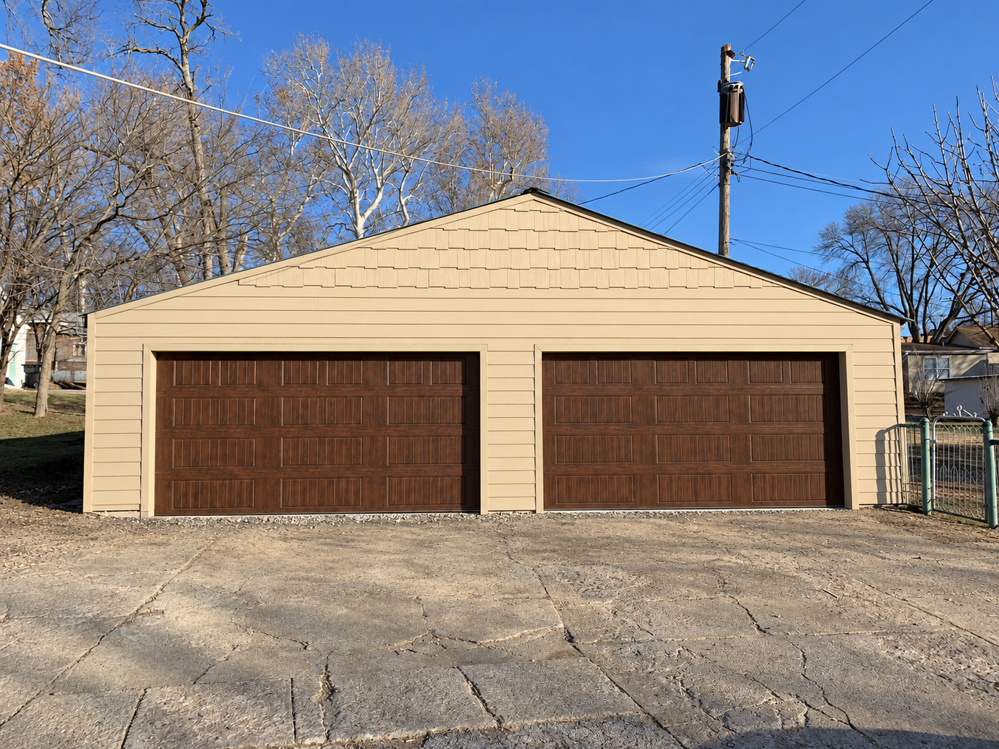 Detached garage with tan siding and two wood-look garage doors