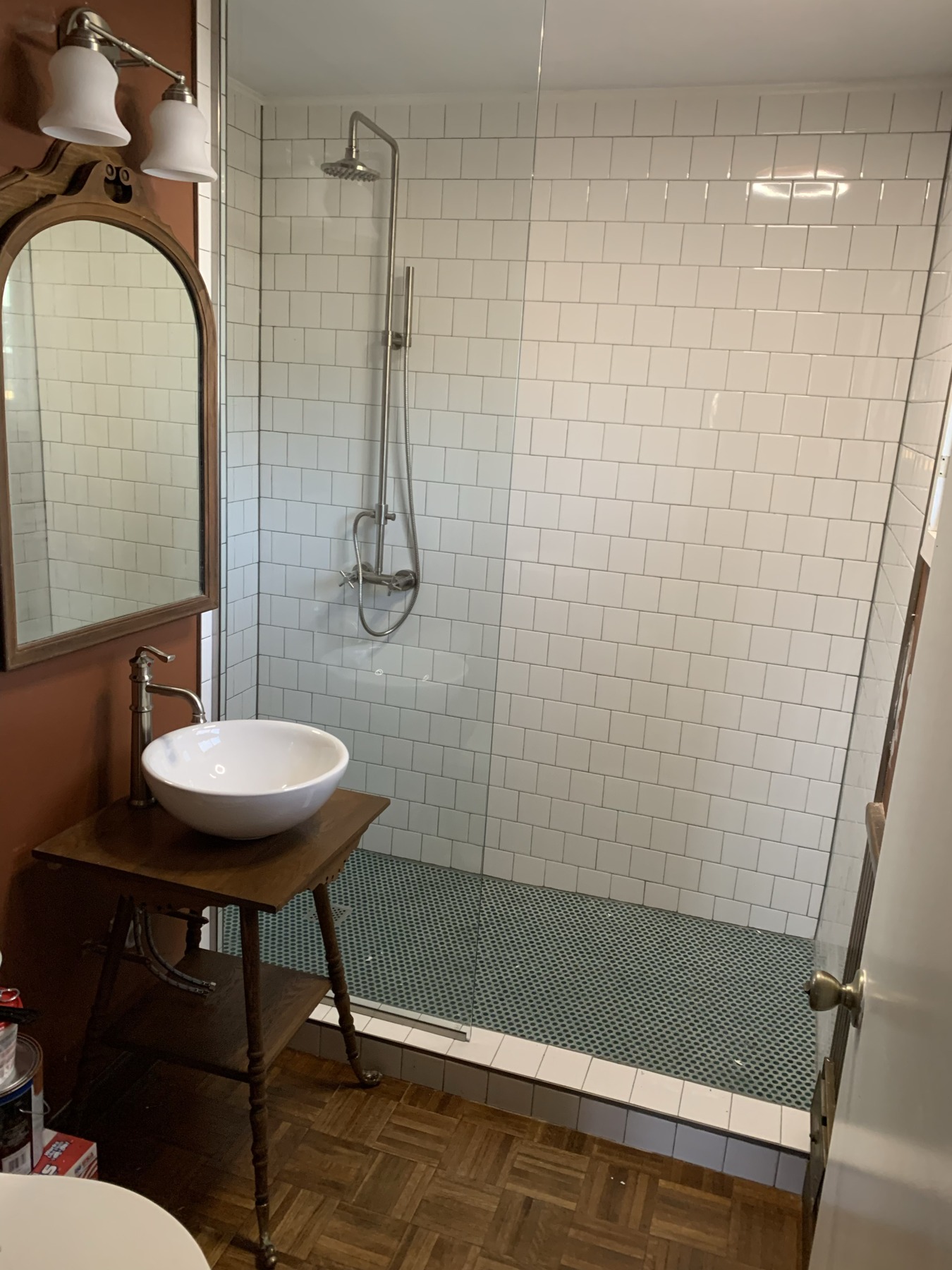 Glass shower enclosure with white tile walls, mosaic flooring, and a vessel sink on a wooden vanity.